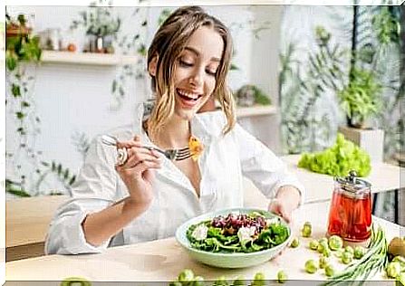 A woman eating a salad smiling. 